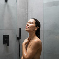 Beautiful woman enjoying a relaxing shower with Watersilks filtered shower head in a modern bathroom, highlighting luxury, wellness, and spa-like water filtration benefits.